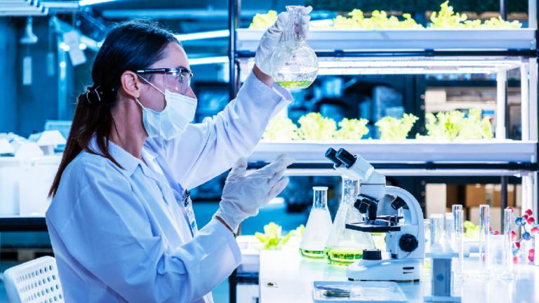 Científica con mascarilla y guantes analiza una muestra en un laboratorio azul iluminado